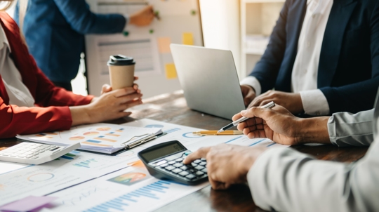 People Looking Over Computers and Calculator