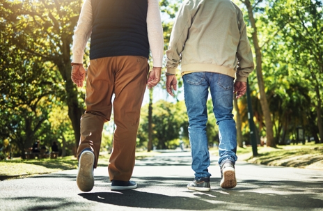 Two adults walking side by side along a tree-lined path on a sunny day. | Adler Law